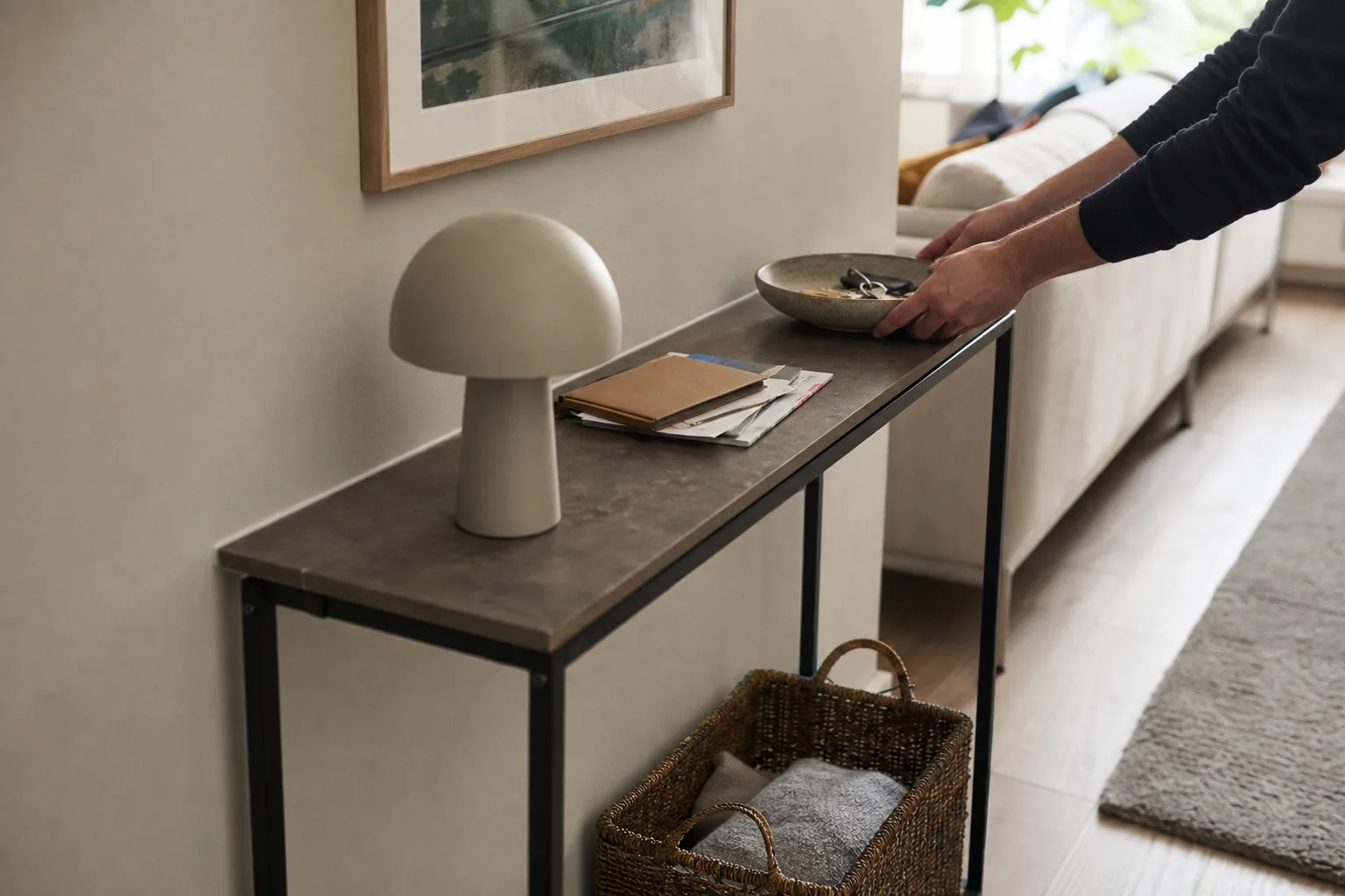 Hand placerar nyckelskål på konsolbord under tavla i vardagsrum